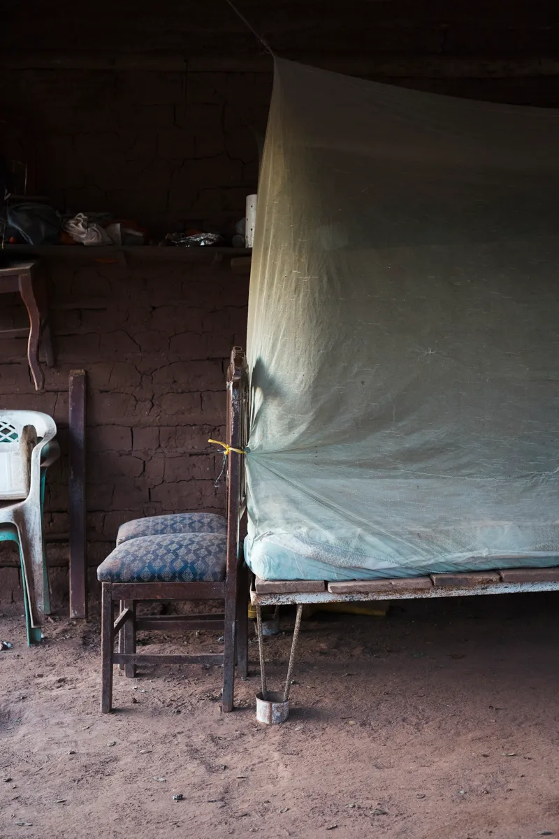 A bed under a mosquito net in a mud-brick room