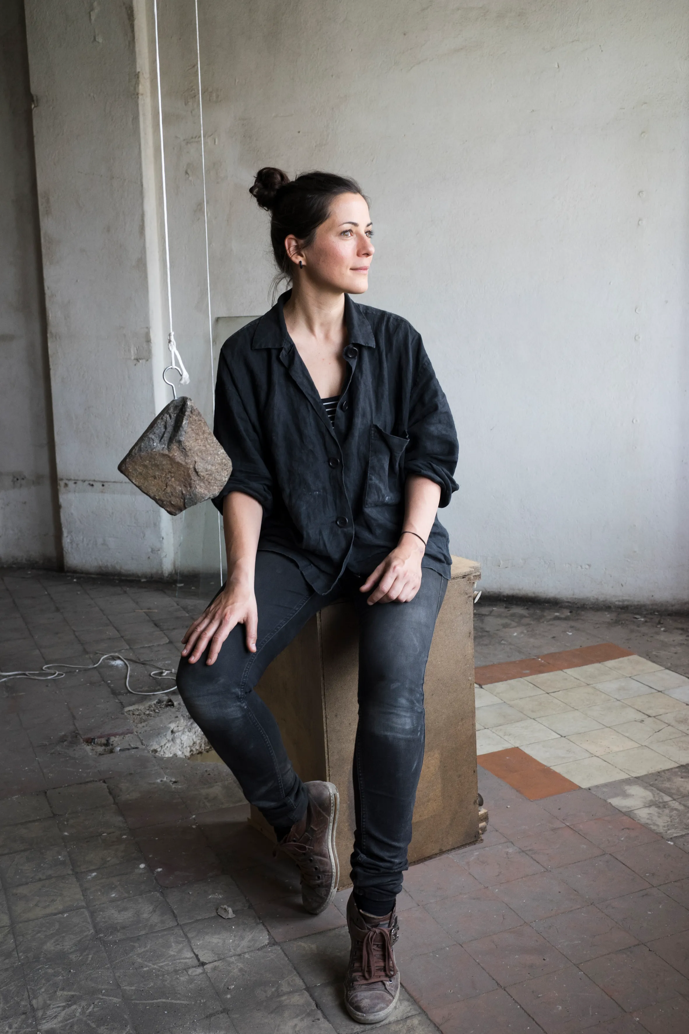 An artist seated beside a suspended stone