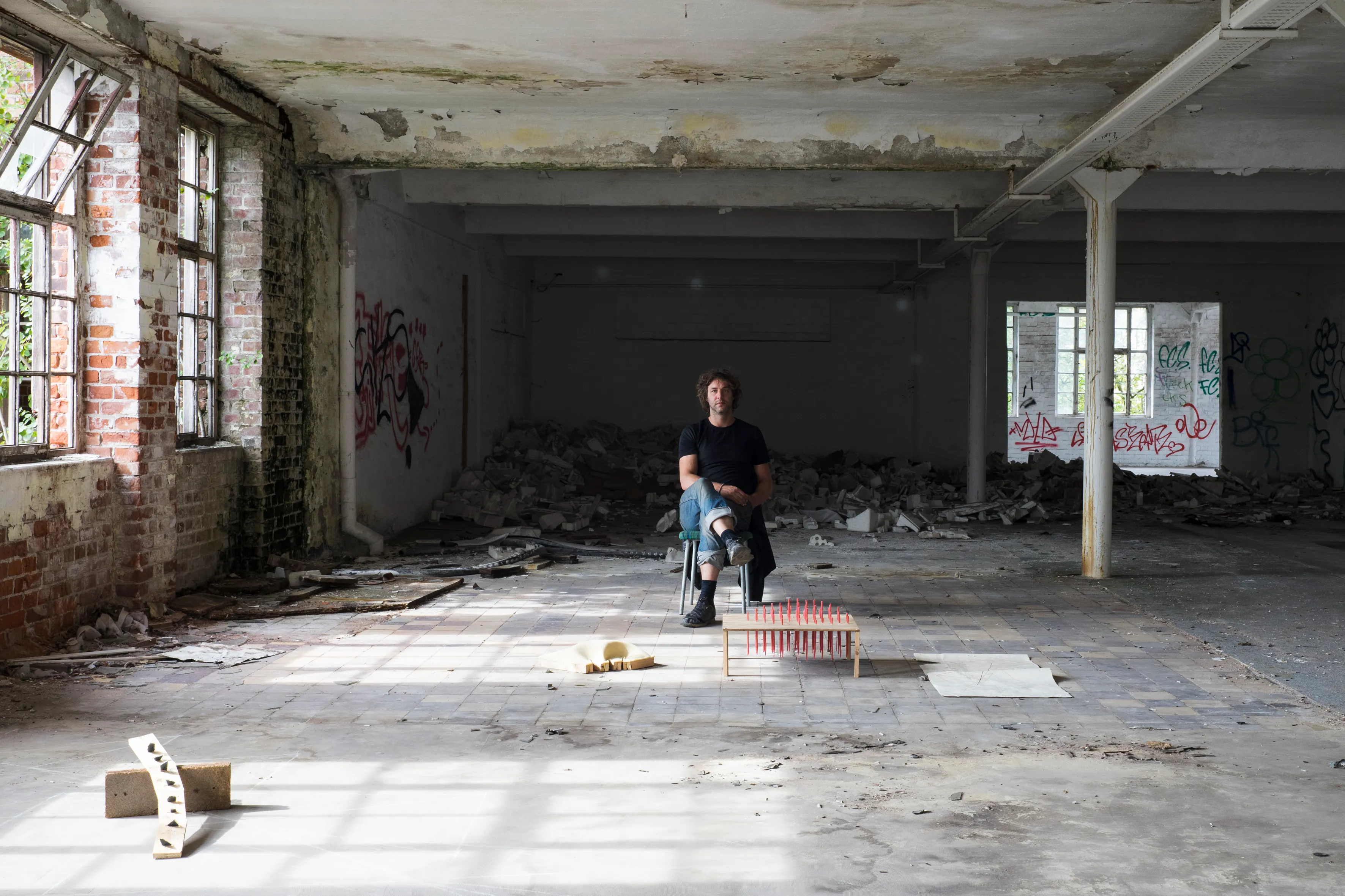 An artist in a graffitied hall with a small floor sculpture