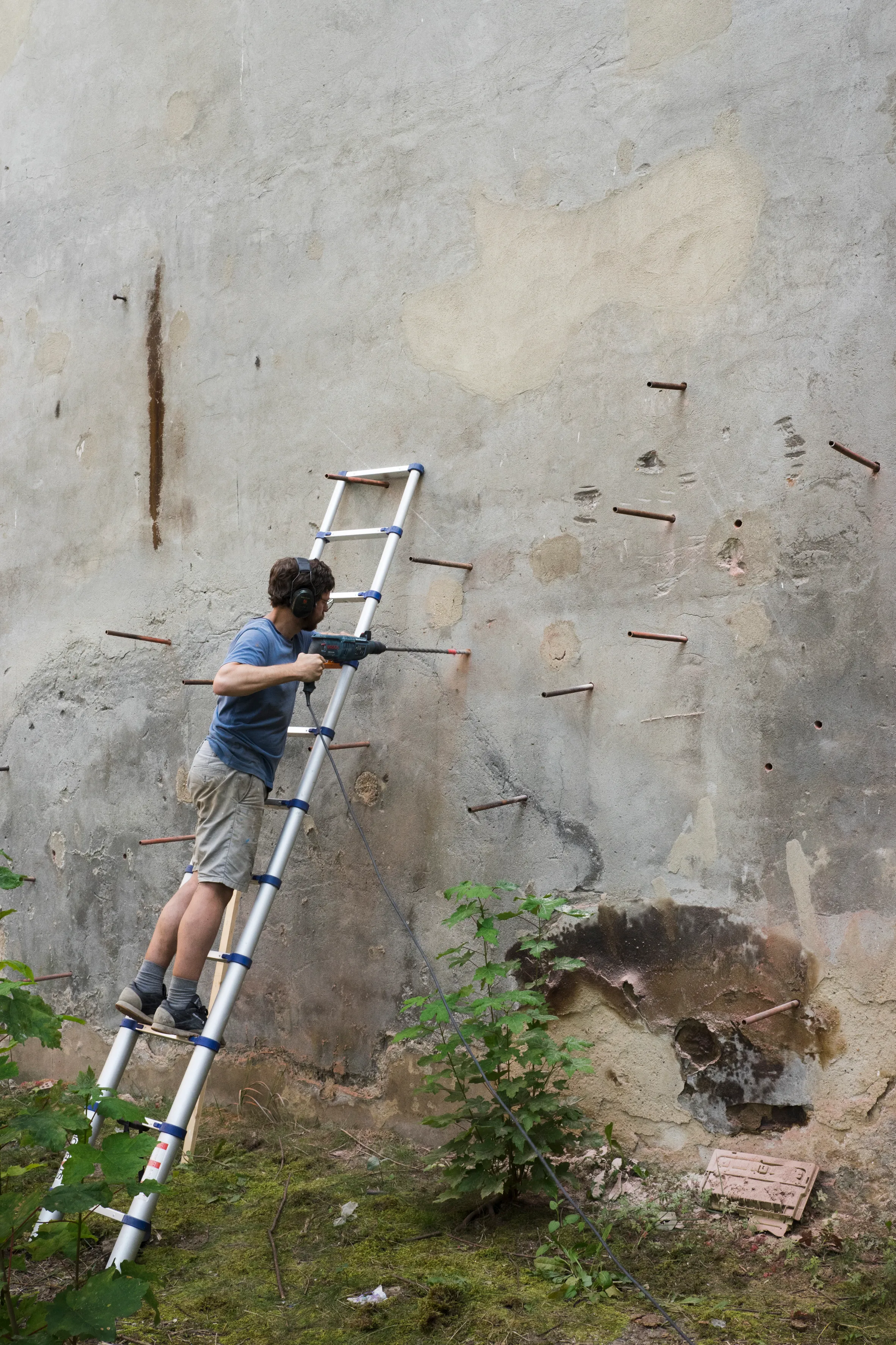 Drilling copper rods into a weathered outdoor wall
