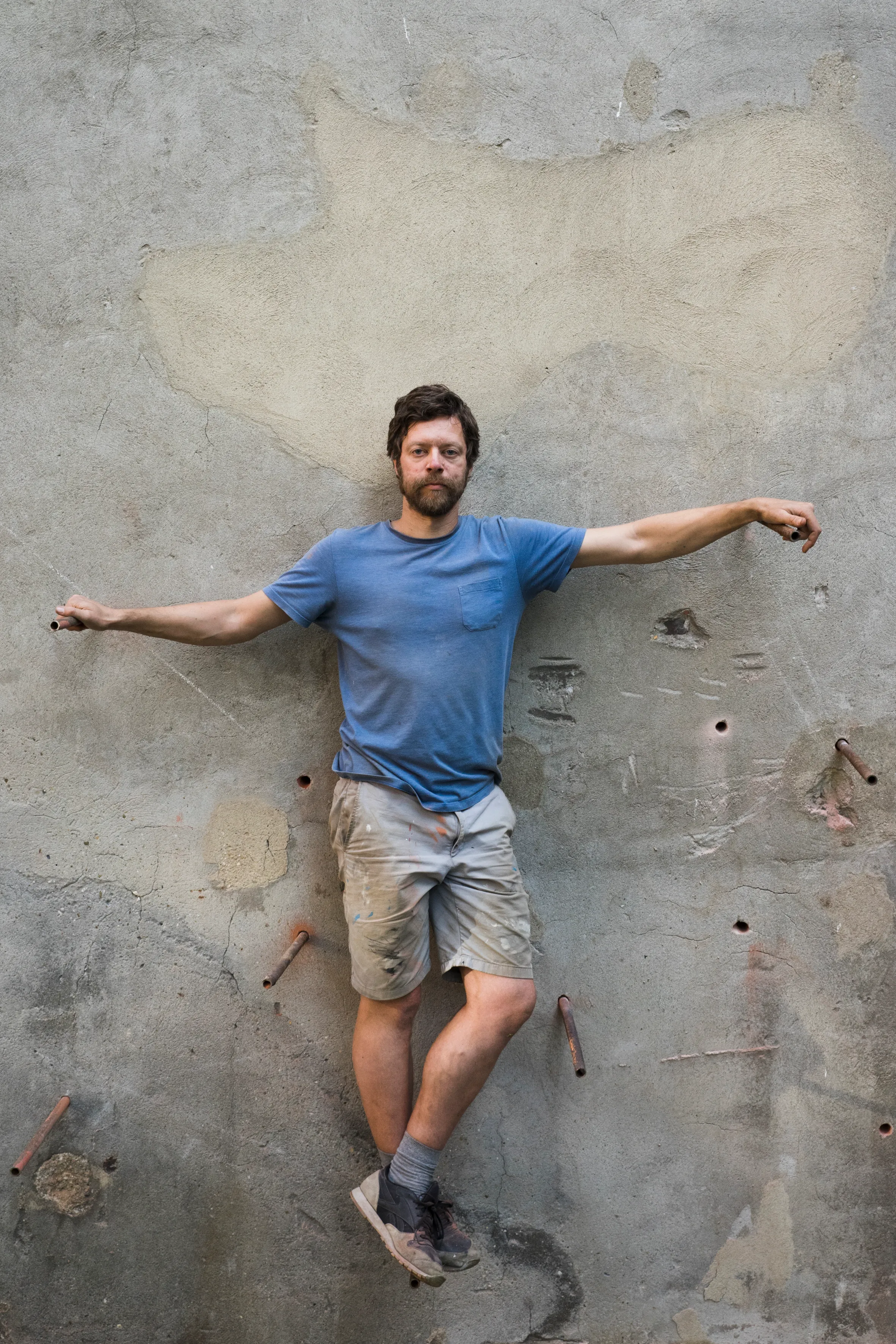 An artist spread against a wall studded with copper rods