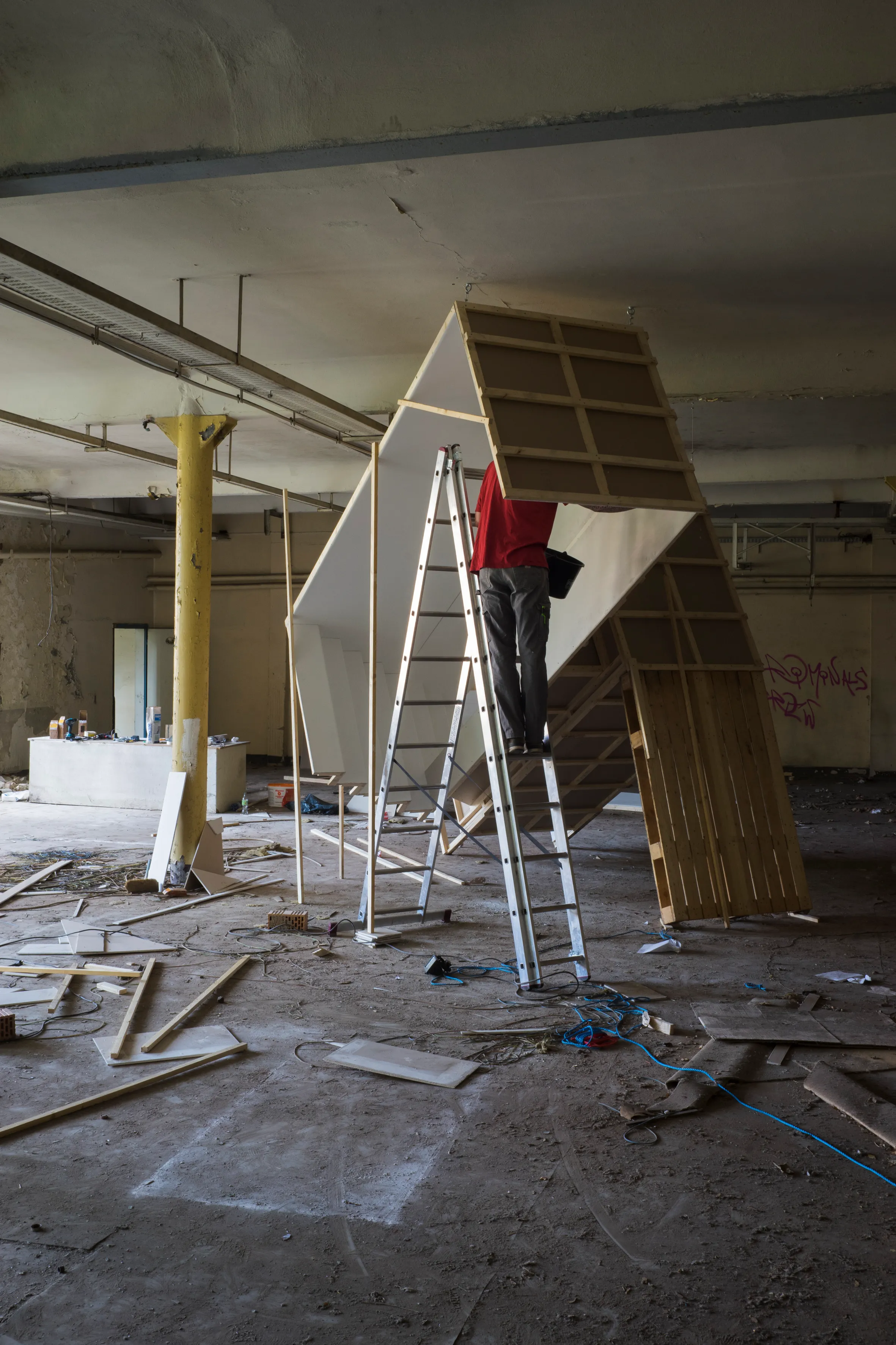 An artist on a ladder building an angular plywood structure