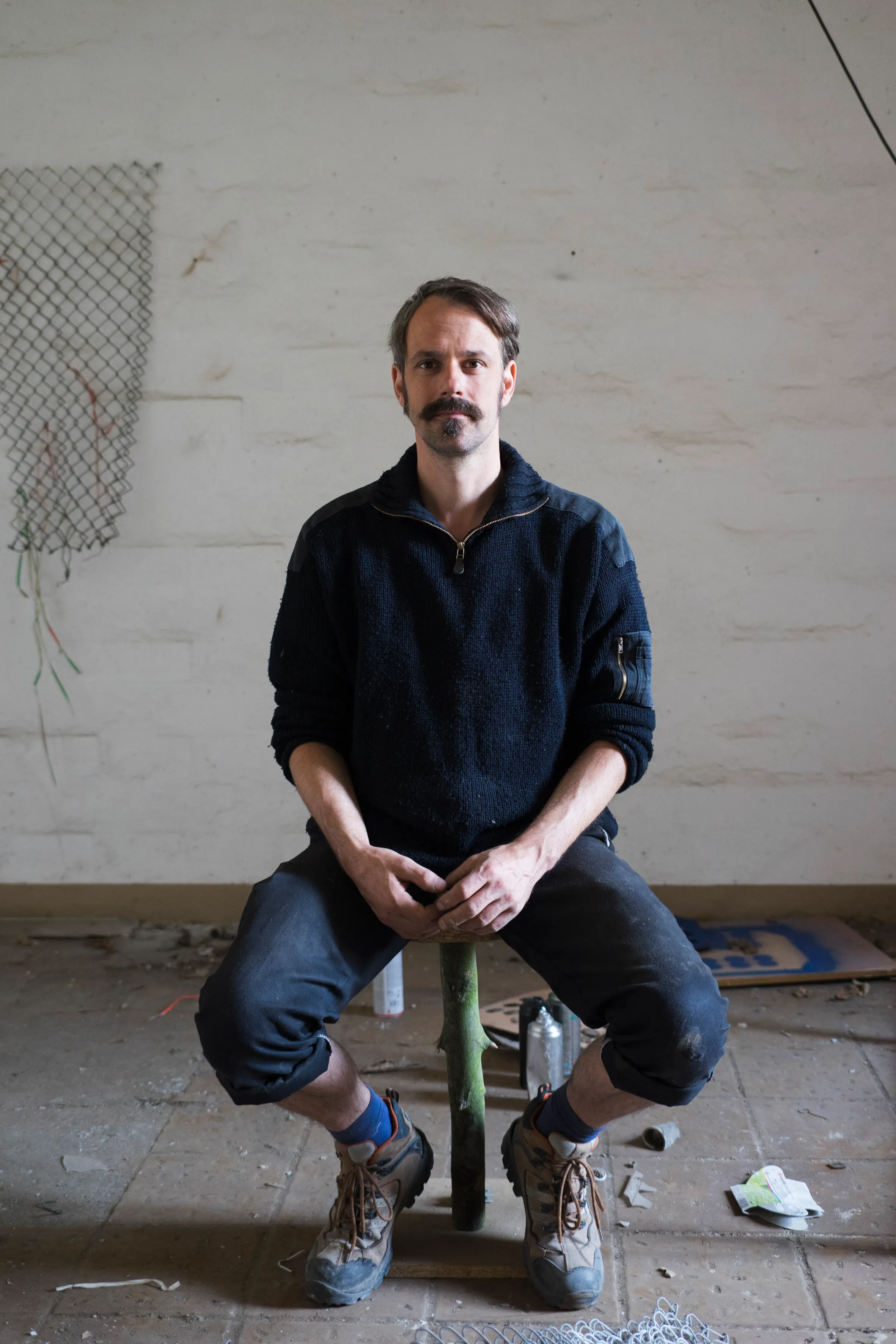 Portrait of an artist beside a chain-link wall work